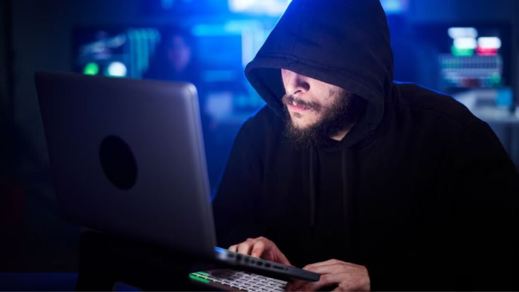 Hacker using laptop in dark room – representing how AIO-TLP tools are fueling a new cybersecurity crisis