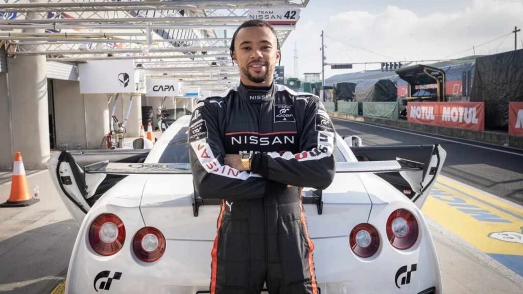 Jann Mardenborough, dressed in a racing suit, stands proudly next to a Nissan car, embodying the spirit of racing.